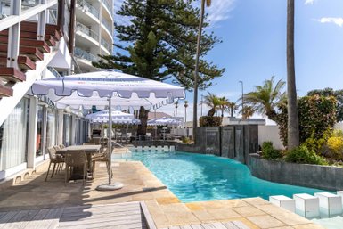 Ein einladender Poolbereich mit Sonnenschirmen und Liegen, umgeben von Palmen und blühenden Pflanzen, strahlt Entspannung aus.