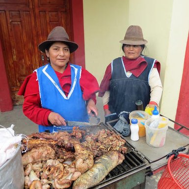 Zwei Frauen in traditioneller Kleidung stehen an einem Grill, während sie köstliches gegrilltes Fleisch zubereiten.