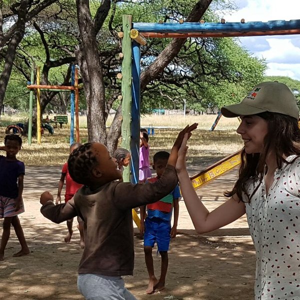 Ein fröhliches Kind mit Zöpfen gibt einem Mädchen einen High Five, während andere Kinder im Hintergrund spielen.
