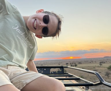 Ein Junge mit Sonnenbrille lächelt fröhlich aus einem Geländewagen, während die Sonne am Horizont untergeht.