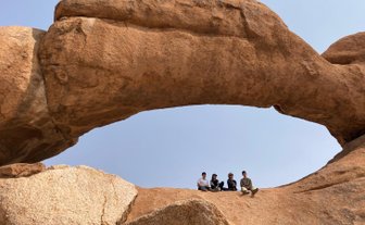 Eine Reisegruppe sitzt gemeinsam unter einem imposanten Felsbogen - Namibia mit Kindern