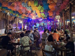 Bunte Papierbanner schmücken die Decke eines lebhaften Lokals, während Gäste an Tischen sitzen und Musik genießen.