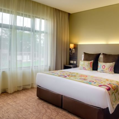 Ein modernes Hotelzimmer mit einem großen Fenster, das Tageslicht hereinlässt, und einem gemütlichen Doppelbett mit buntem Überwurf.