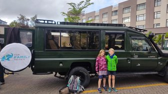 Zwei Kinder stehen lächelnd neben einem grünen Jeep, bereit für ein Abenteuer in der Natur.