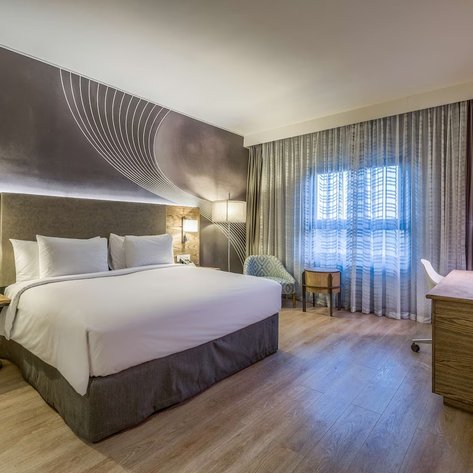 Ein modernes Hotelzimmer mit einem großen Bett, eleganten Möbeln und einem Fenster, das Tageslicht hereinlässt.