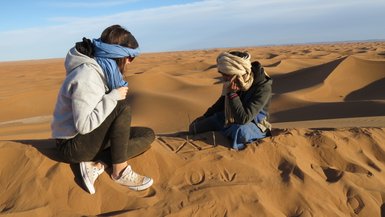 Guide sitzt mit einer Touristin auf einer Sanddüne der Sahara – Marokko Reise mit Kindern