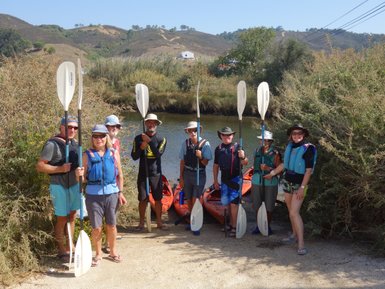 Eine Gruppe von sieben Kajakfahrern steht am Ufer eines ruhigen Gewässers, bereit für ein Abenteuer in der Natur.