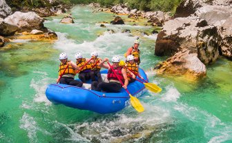 Eine Gruppe von sechs Personen paddelt in einem blauen Raft durch einen klaren, grünen Fluss, umgeben von Felsen und Bäumen.