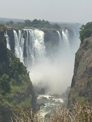 Die majestätischen Victoriafälle stürzen in einen nebligen Abgrund, umgeben von üppigem Grün und steilen Klippen.