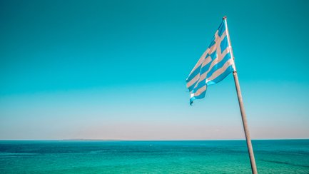 Eine griechische Flagge weht sanft über dem klaren, blauen Wasser des Meeres unter einem strahlend blauen Himmel.