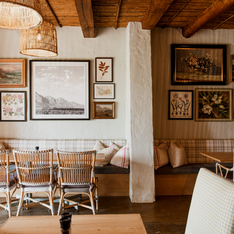 Ein gemütlicher Restaurantbereich mit Rattanmöbeln, dekoriert mit verschiedenen Kunstwerken an den Wänden.