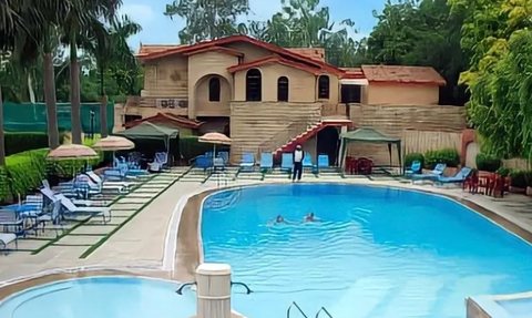 Ein einladender Poolbereich mit Liegen und Sonnenschirmen, umgeben von üppigem Grün und einem charmanten Gebäude im Hintergrund.