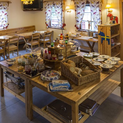 Ein einladender Frühstücksraum mit Holztischen, einem reichhaltigen Buffet und bunten Vorhängen, die eine gemütliche Atmosphäre schaffen.