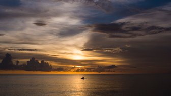 Ein einzelner Paddler gleitet ruhig über das glitzernde Wasser, während die Sonne hinter dem Horizont untergeht.