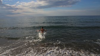 Ein Junge mit nacktem Oberkörper springt fröhlich ins Wasser, während Wellen sanft an den Strand rollen.
