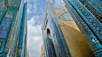 Blick auf die kunstvoll verzierten Wände des Shah-i-Zinda Komplexes in Samarkand, umgeben von strahlend blauem Himmel.