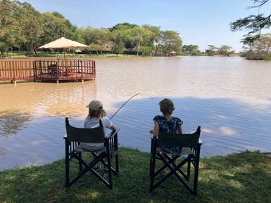 Zwei Kinder sitzen auf Klappstühlen am Ufer eines ruhigen Sees und beobachten die Wasseroberfläche mit Angeln in der Hand.