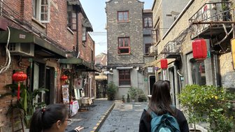 Eine Frau mit einem Rucksack steht in einer schmalen Gasse, umgeben von historischen Backsteingebäuden und roten Laternen.