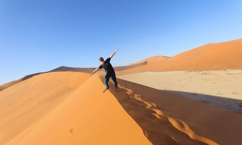 Ein Junge steht auf dem Kamm einer Sanddüne in der Wüste - Namibia Urlaub mit Kindern