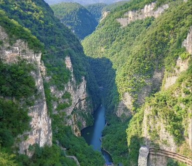 Eine atemberaubende Aussicht auf die tiefen, bewaldeten Schluchten des Zhangjiajie Grand Canyon mit einem ruhigen Fluss in der Mitte.