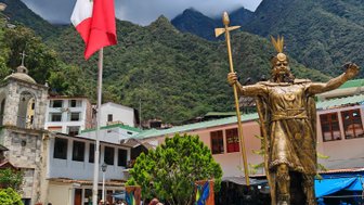 Eine goldene Statue eines Inka-Herrschers steht stolz vor den majestätischen Anden, umgeben von einem lebhaften Dorf.
