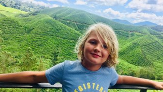 Kind steht lächelnd vor der Hügellandschaft der Cameron Highlands – Malaysia & Borneo Reise mit Kindern