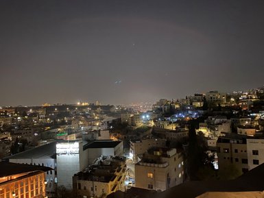 Die nächtliche Stadtansicht von Amman zeigt beleuchtete Gebäude und sanfte Hügel, die in der Dunkelheit schimmern.