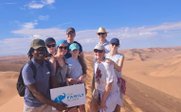 Reisegruppe hält in der Wüste Schild mit For Family Reisen - Namibia Family & Teens - Namibia mit Jugendlichen