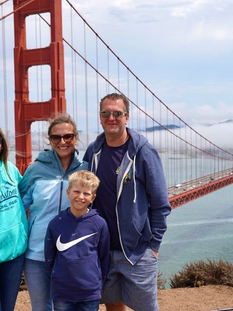 Eine Familie posiert fröhlich vor der Golden Gate Bridge, umgeben von einer malerischen Küstenlandschaft und sanften Wolken.