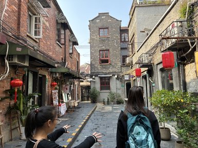 Eine Frau mit einem Rucksack steht in einer schmalen Gasse, umgeben von historischen Backsteingebäuden und roten Laternen.