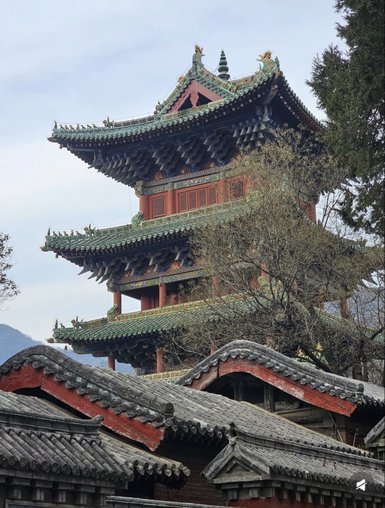 Ein majestätischer Pagodenturm mit kunstvollen Dachdetails erhebt sich über traditionelle, rote Gebäude im Vordergrund.