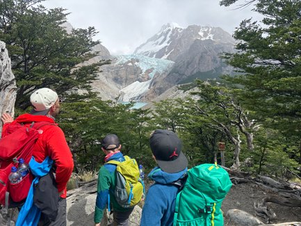 Drei Wanderer stehen auf einem Pfad und blicken auf einen beeindruckenden Gletscher in den Bergen von Patagonien.