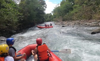 Eine Gruppe von Menschen in einem roten Schlauchboot paddelt durch einen ruhigen Fluss, umgeben von üppigem Grün.
