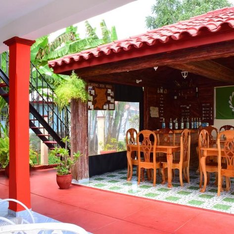 Ein einladendes Restaurant mit Holztischen und Stühlen, umgeben von üppigem Grün und einem roten Dach.