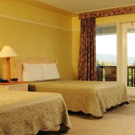 Ein helles Hotelzimmer mit zwei Einzelbetten, eleganten Bettdecken und einem Balkon mit Blick auf die Natur.