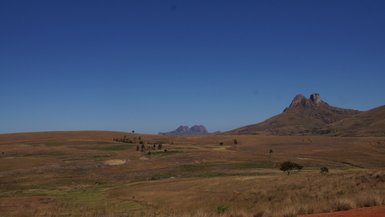 Eine weite, trockene Landschaft mit sanften Hügeln und einem klaren blauen Himmel, der die Szenerie erhellt.
