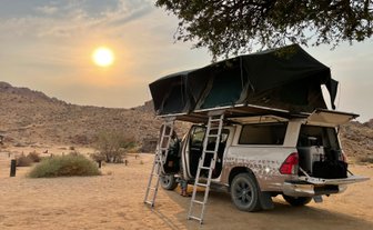 Ein Jeep steht mit aufgebautem Dachzelt auf einer Sandfläche