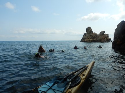 Eine Gruppe von Schwimmern erkundet das klare Wasser, während ein Kajak im Vordergrund liegt und Felsen im Hintergrund sichtbar sind.