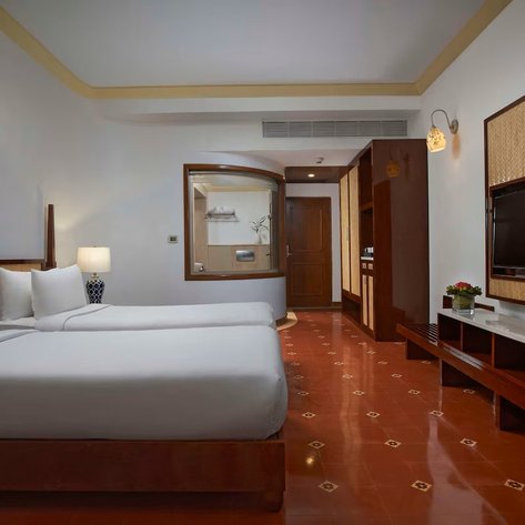 Ein modernes Hotelzimmer mit zwei Einzelbetten, eleganten Möbeln und einem großen Fernseher an der Wand.