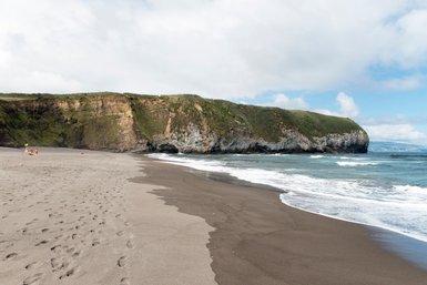 Ein ruhiger Strand mit sanften Wellen, umgeben von steilen Klippen und üppigem Grün, lädt zum Entspannen ein.