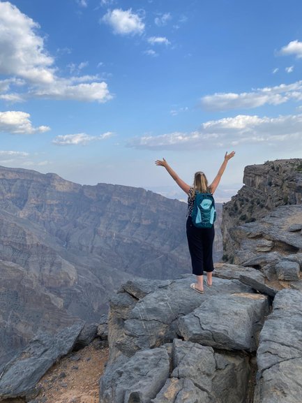 Frau steht auf einem Felsen und genießt die Aussicht über die Schluchten des Jebel Shams – Oman mit Kindern