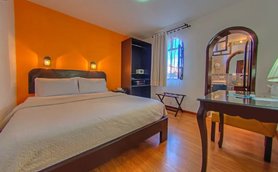 Ein gemütliches Hotelzimmer mit einem großen Bett, orangefarbener Wand und warmem Licht von Wandlampen.