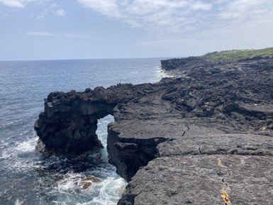 Eine beeindruckende Küstenlandschaft mit schwarzem Lavagestein, das ins Meer ragt und von Wellen umspült wird.