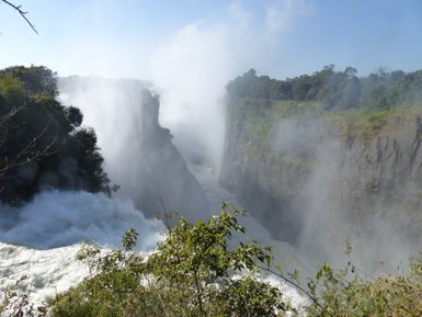 Die majestätischen Victoriafälle stürzen in die Tiefe, umgeben von üppigem Grün und einem Nebel aus Wassertröpfchen.