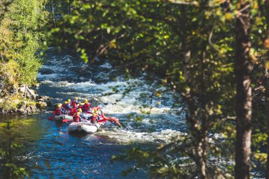 Eine Gruppe von Menschen in roten Schwimmwesten paddelt in einem Schlauchboot auf einem rauschenden Fluss.
