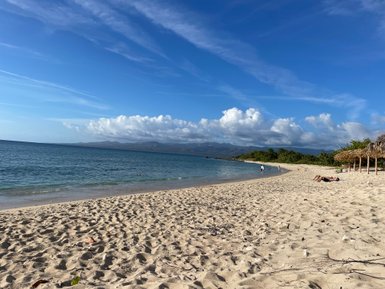 Ein ruhiger Strand mit feinem Sand, sanften Wellen und einer malerischen Küstenlinie unter einem strahlend blauen Himmel.