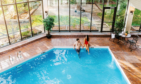 Ein Paar steht im Wasser eines Innenpools, umgeben von großen Fenstern und einem hellen, einladenden Raum.