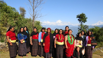 Eine Gruppe von Frauen aus Bhakunde steht in traditioneller Kleidung vor einer beeindruckenden Berglandschaft.