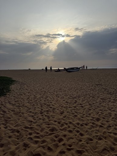 Am Strand von Negombo stehen Menschen vor einem dramatischen Himmel, während die Sonne durch die Wolken strahlt.
