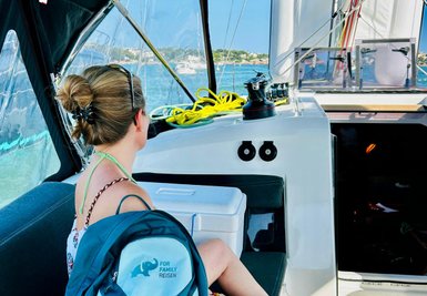 Eine Frau sitzt auf einem Boot und blickt auf das Wasser, während sie einen blauen Rucksack neben sich hat.